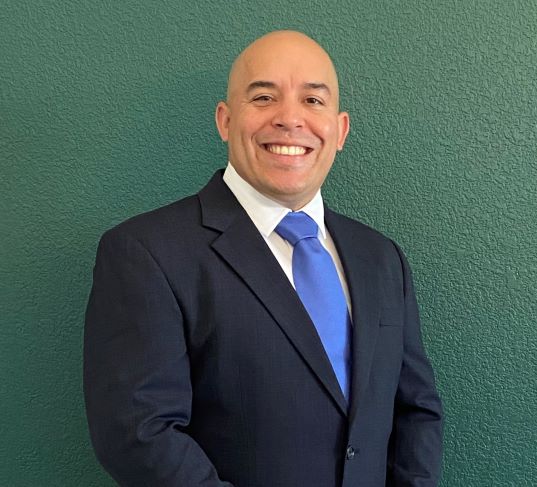 A Caucasian man in a business suit in front of a green wall.